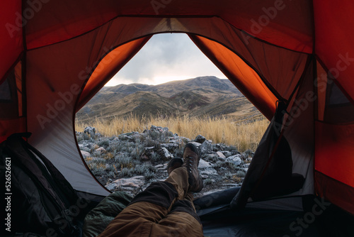 man's feet with boots inside an orange tent in the mountains in a sunset surrounded by rocks and yellow vegetation in the winter in the andes mountain range