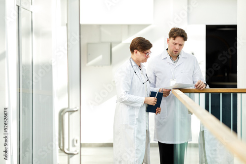 Minimal portrait of two expert doctors discussing case in hall of modern clinic in white tones, copy space