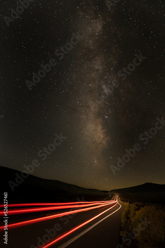 Long exposure traffic trails from tail lights stretching down the road toward the milky way