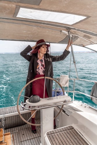 Attractive middle-aged woman at the helm of a yacht on a summer day. Luxury summer adventure, outdoor activities. © svetograph