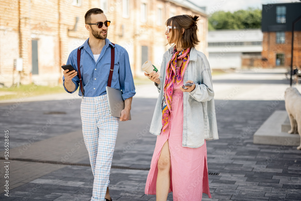 Young stylish couple have some conversation while walking together during a coffee break. Young hipsters hang out together near office outdoors