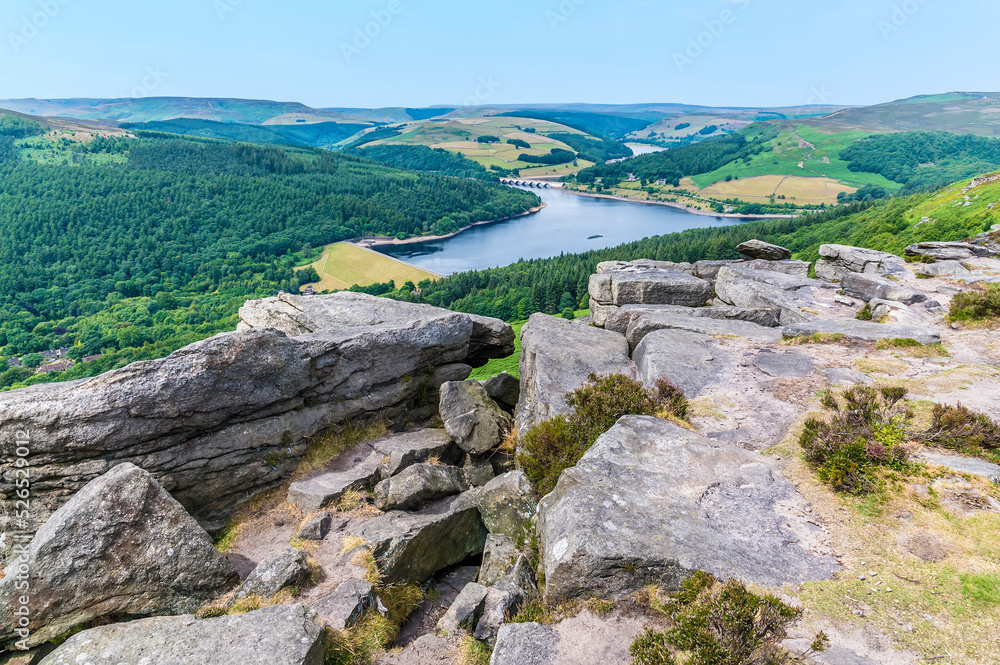 A view over boulders and the cliff edge of Bamford Edge towards Ladybower reservoir, UK in summertime