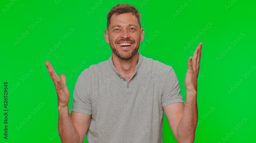 Fototapeta premium Happy handsome young man shouting, raising fists in gesture I did it, celebrating success, winning, birthday, lottery goal achievemen. Adult guy isolated on green chroma key studio background indoors