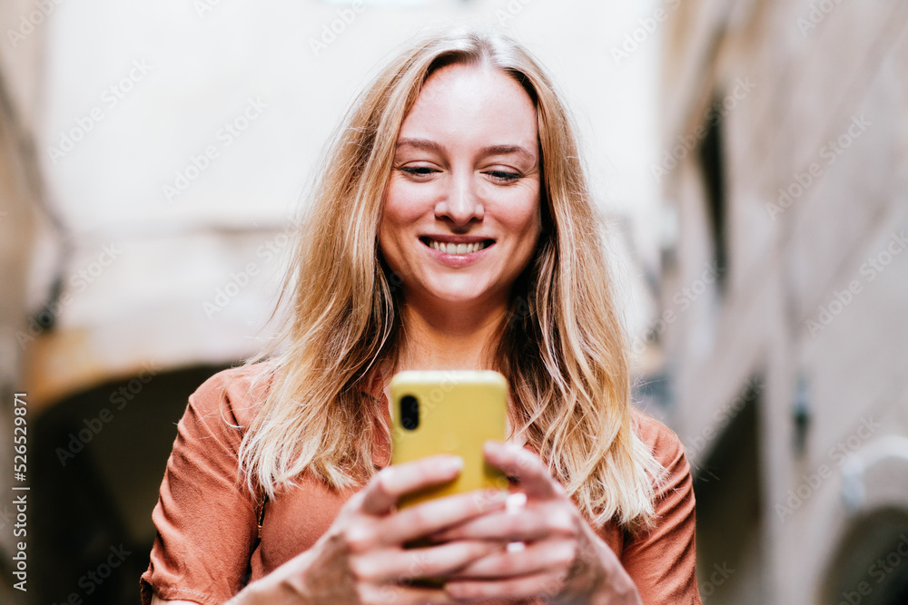 attractive young blonde woman smiling while using her smart phone in the street attractive young blonde woman smiling while using her smart phone in the street