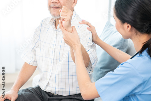 Caring young female doctor performing osteopathy treatment for a contented senior patient. At-home medical treatment for an Asian senior patient, joint pain treatment, medical service for seniors.