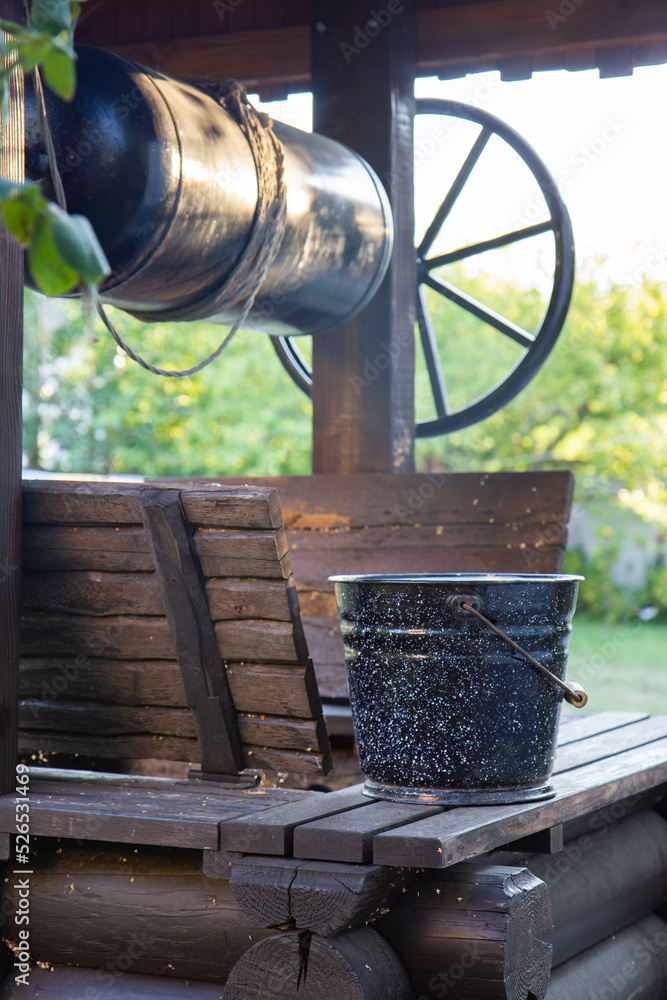 rural wooden well and black bucket of water