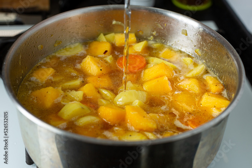 Water is poured into a saucepan with fried vegetables to make pumpkin soup