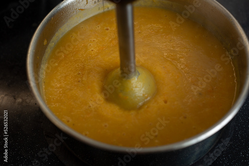 In a saucepan with an immersion blender, cooked vegetables are interrupted in a soup puree