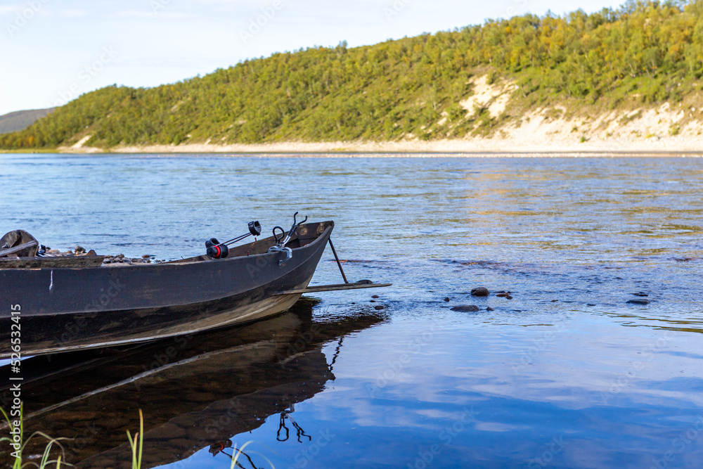 A wooden fishing boat in the Teno river in Lapland, Finland, with white sand and forest on the opposite bank in the background. Teno has been praised as one of the best salmon rivers in Europe.