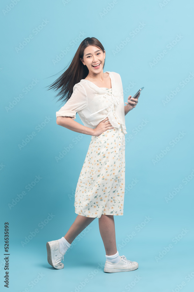 Beautiful young asian woman in white dress with flower pattern using smartphone isolated on blue background Beautiful young asian woman in white dress with flower pattern using smartphone isolated on blue background