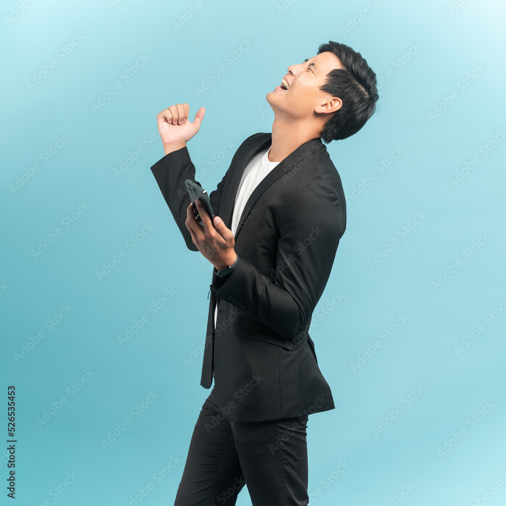 Good looking businessman portrait using smartphone with very excited emotion isolated on blue background Good looking businessman portrait using smartphone with very excited emotion isolated on blue background