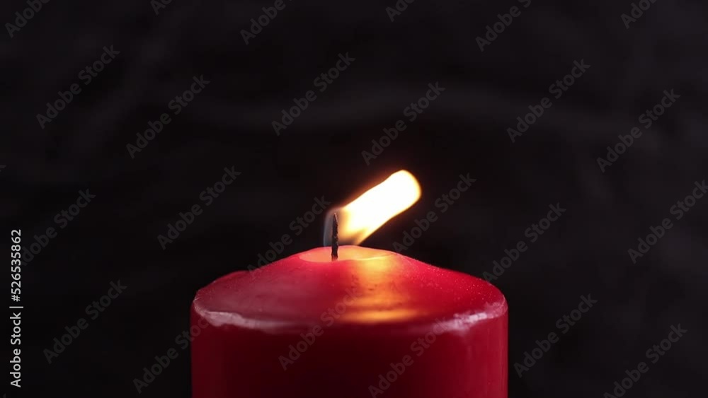 A stream of air blows out a large red candle, smoke from the wick, black background A stream of air blows out a large red candle, smoke from the wick, black background