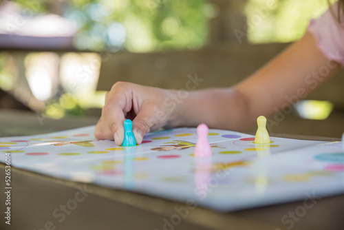 Board game and kids leisure concept - little girl hold figure in hand. yellow, blue, pink chips in children play.Table game. Movement. The girl moves the chip. Victory.
