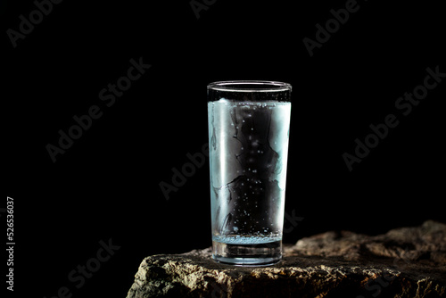 a glass of water with walls fogged up from the cold on a rock on a black background