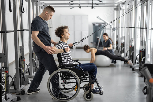 Murais de parede Rehabilitation specialist helps a guy in a wheelchair to do exercise on decompression simulator for recovery from injury