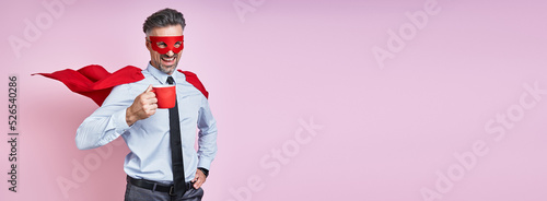 Cheerful man in shirt and tie wearing superhero cape and holding coffee cup against pink background