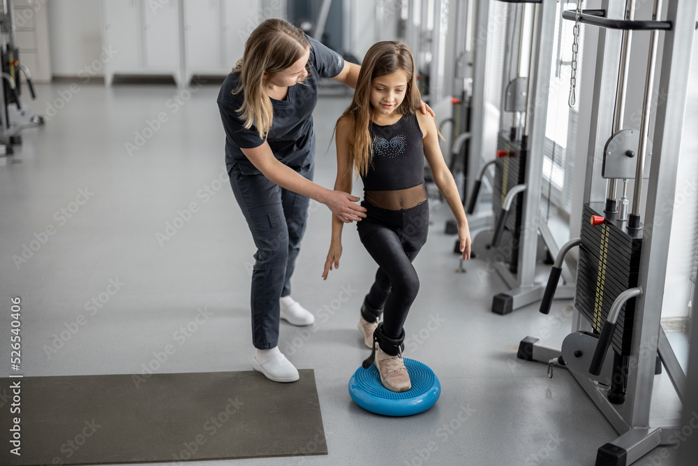 Rehabilitation specialist helping little girl to do exercises at gym