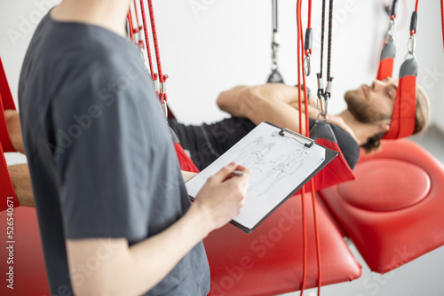 Rehabilitation specialist examining male patient before active treatment on suspension straps. Therapeutic exercises and neuromuscular activation on red cord slings photo