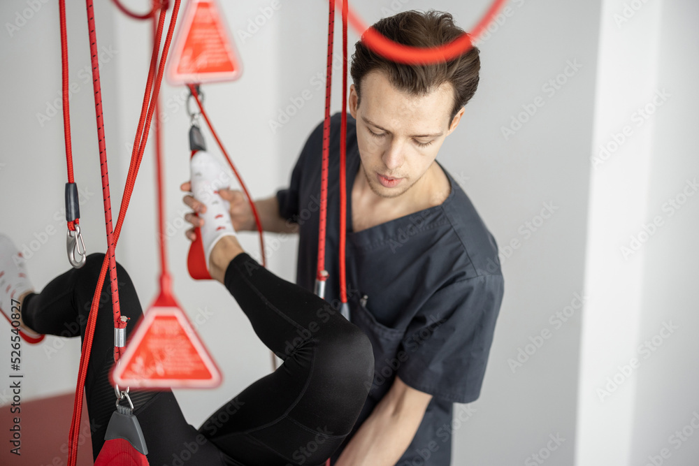 Rehabilitation specialist doing active treatment on suspension straps to female patient. Concept of therapeutic exercises to restore pain-free movement patterns and improve function Rehabilitation specialist doing active treatment on suspension straps to female patient. Concept of therapeutic exercises to restore pain-free movement patterns and improve function