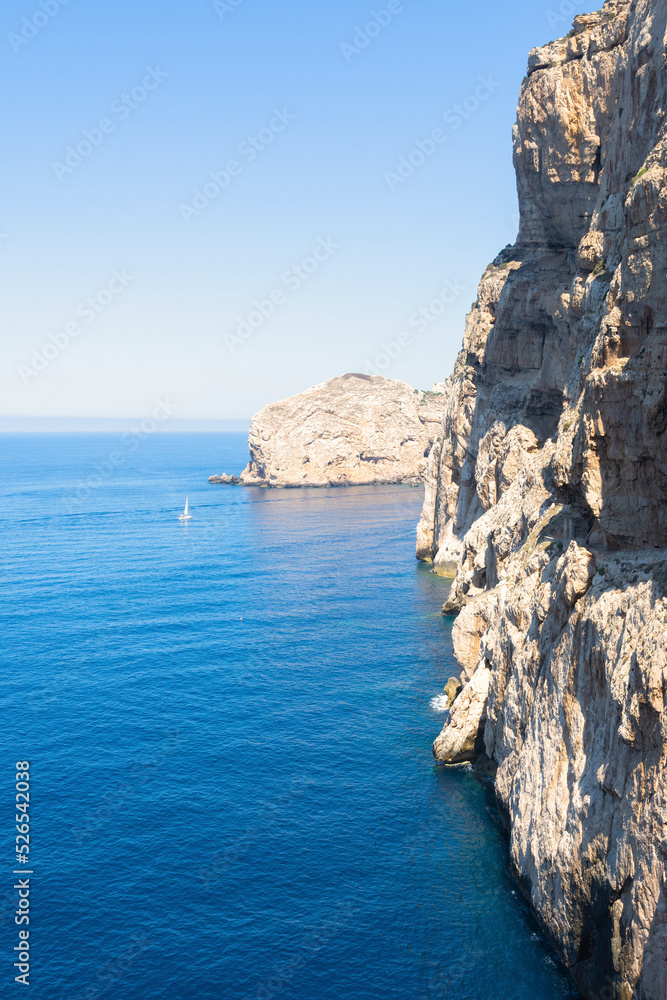 Vertical view from a gorge with a white rock corridor, in the background a sailboat with a turquoise Mediterranean Sea.