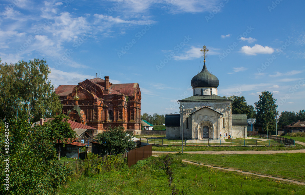 Yuryev-Polsky, Vladimir Region, Russia - August, 17, 2022: the white-stone St. George Church and the brick church of the Holy Trinity on a clear sunny summer day in the old town