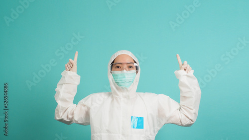 Asian woman in PPE suit wears face mask is pointing fingers up on green or Tiffany Blue backgrounds.