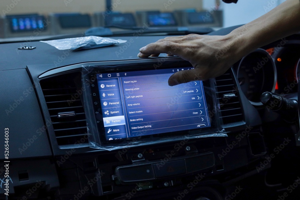 A cropped hand adjusting the in-car display system. Noise and luminance are visible due to low light and high ISO
