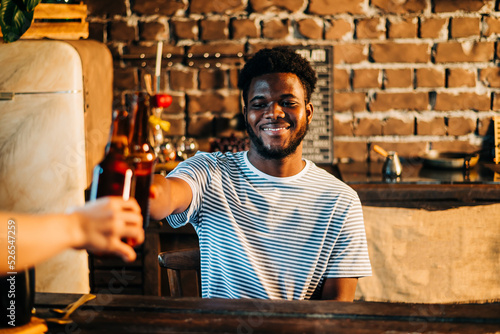 Tableau sur toile Shot of attractive african young happy smiling man drinking beer bottle in the bar close up portrait