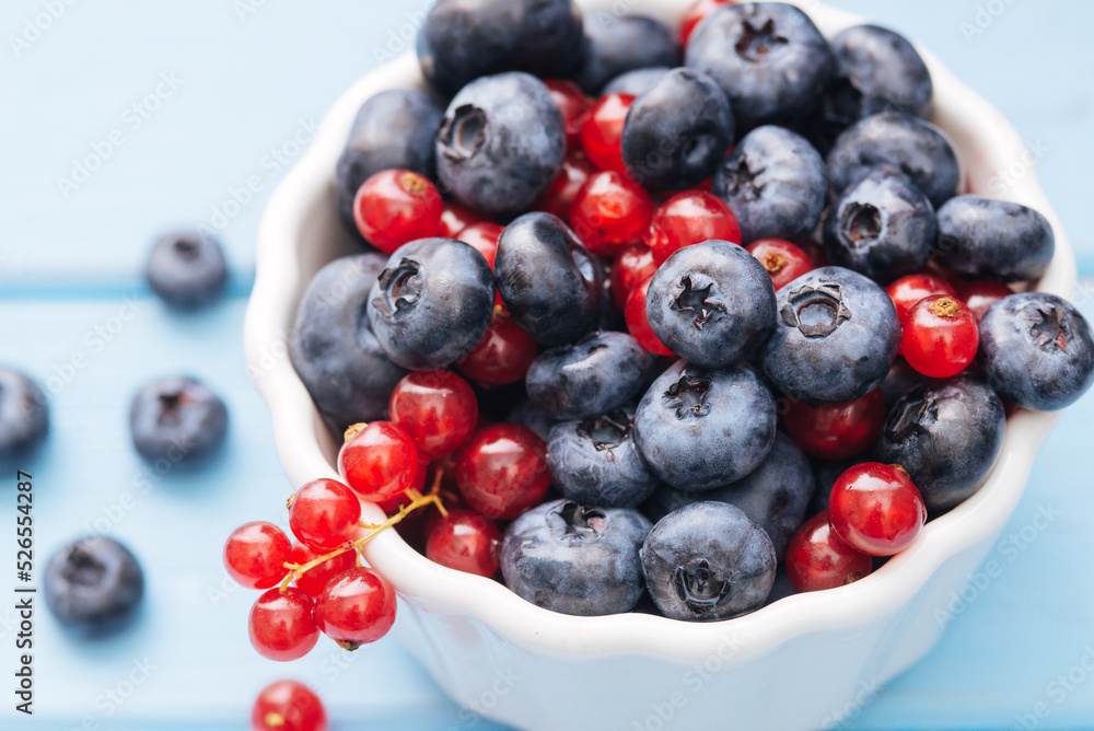 Assorted berries in white bowl on wood: blueberry and red currant on blue wood background. Summer Freshly Berry Assorted berries in white bowl on wood: blueberry and red currant on blue wood background. Summer Freshly Berry