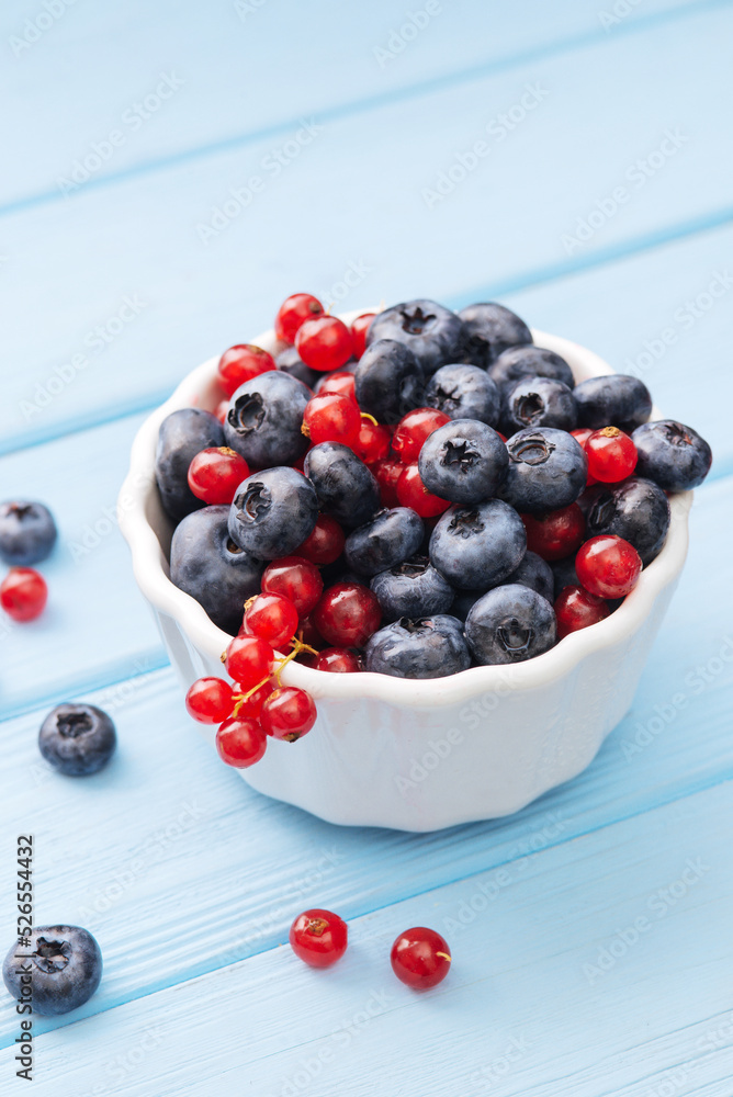 Assorted berries in white bowl on wood: blueberry and red currant on blue wood background. Summer Freshly Berry Assorted berries in white bowl on wood: blueberry and red currant on blue wood background. Summer Freshly Berry