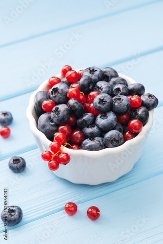 Assorted berries in white bowl on wood: blueberry and red currant on blue wood background. Summer Freshly Berry