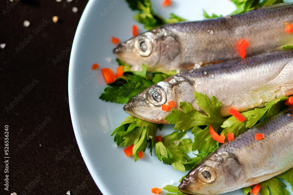 Three small fried herrings on a blue plate on a black background. Three small fried herrings on a blue plate on a black background.