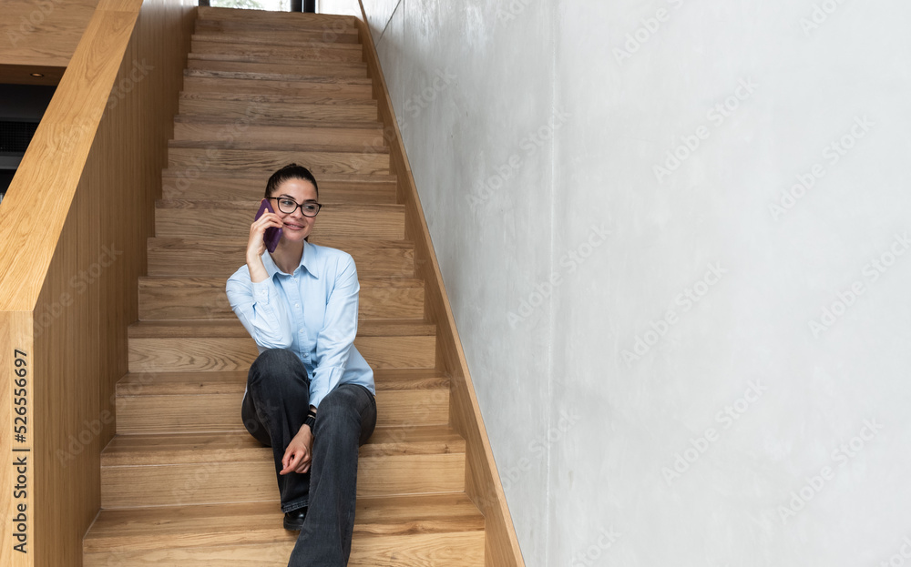 Young expert business woman sitting at the staircase texting and calling her boss to tell that the meeting was well and the deal was signed. Happy female in smart casual sending message on smartphone. Young expert business woman sitting at the staircase texting and calling her boss to tell that the meeting was well and the deal was signed. Happy female in smart casual sending message on smartphone.