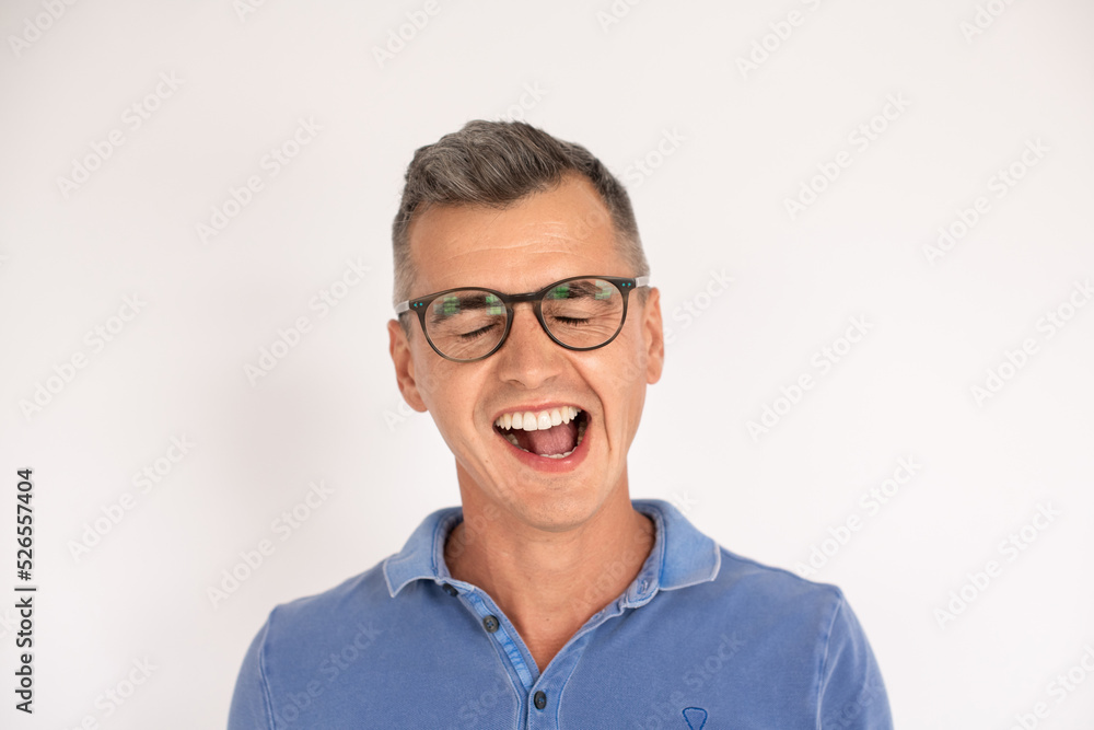 Funny mature man wearing glasses and yawning with closed eyes. Caucasian man wearing blue T-shirt standing with open mouth over white background. Making faces concept