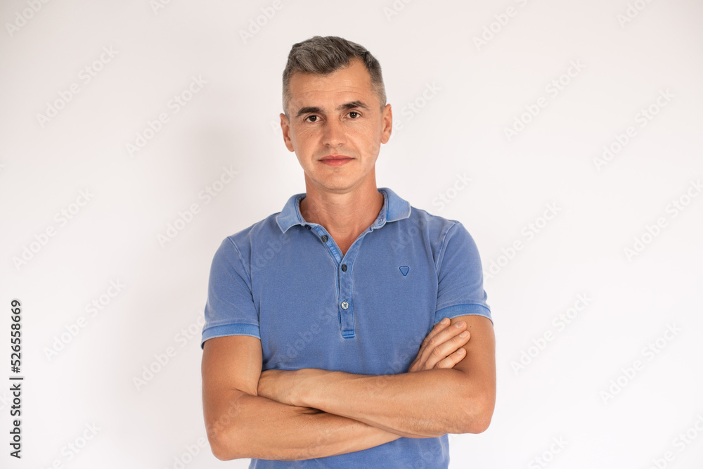 Portrait of confident mature man standing with folded arms. Caucasian man wearing blue T-shirt standing and looking at camera over white background. Confidence concept Portrait of confident mature man standing with folded arms. Caucasian man wearing blue T-shirt standing and looking at camera over white background. Confidence concept