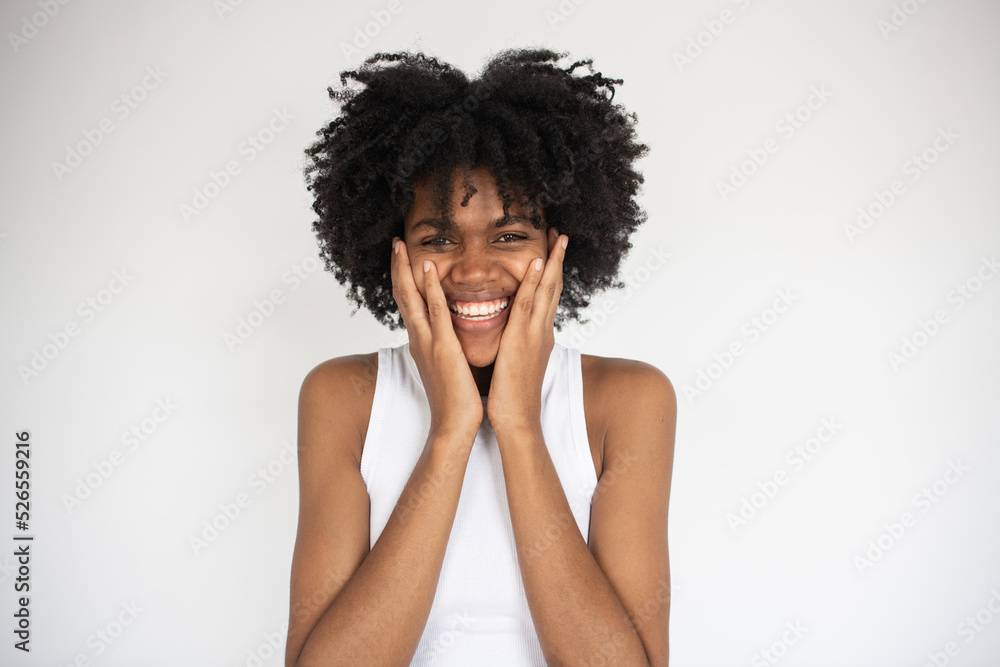 Portrait of happy young woman holding head in hands. Young African American woman wearing white top looking at camera. Admiration and surprise concept Portrait of happy young woman holding head in hands. Young African American woman wearing white top looking at camera. Admiration and surprise concept