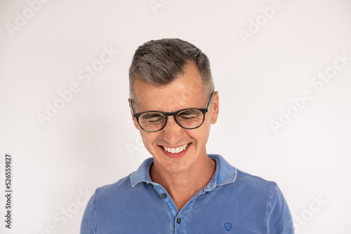 Portrait of laughing mature man wearing glasses. Happy Caucasian man wearing blue T-shirt standing over white background. Humor concept