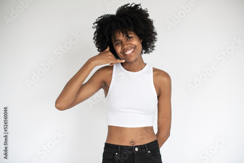Portrait of happy African American woman making phone gesture. Young female model wearing white crop top and jeans looking at camera and smiling. Contact us concept