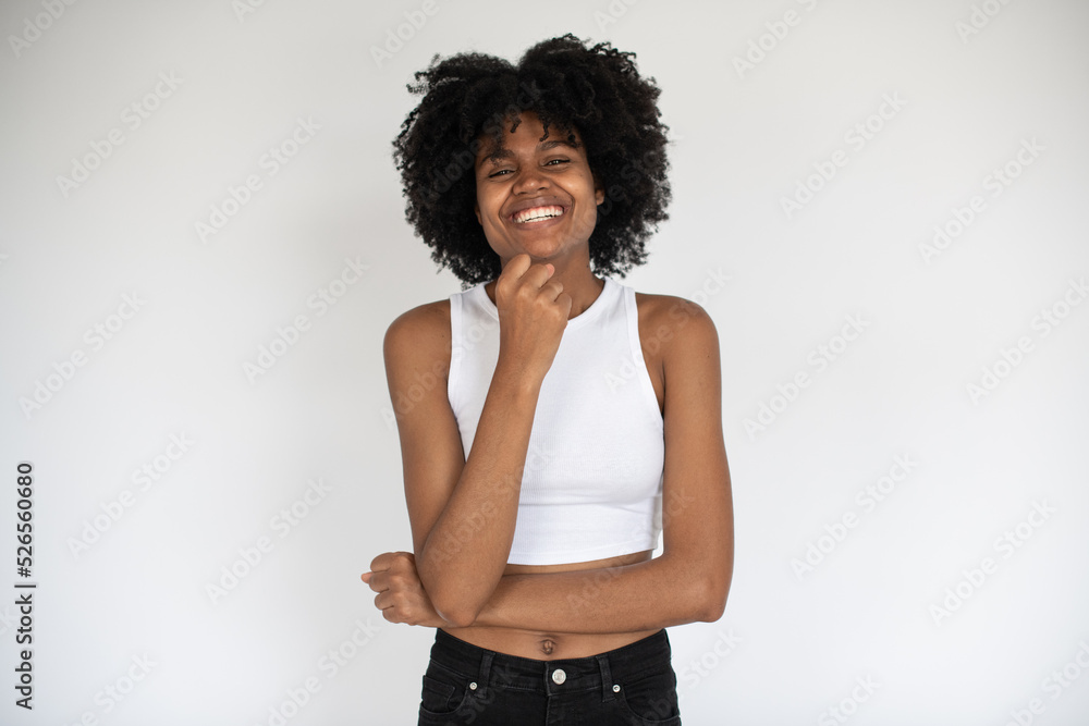 Portrait of cheerful African American woman smiling at camera. Young girl wearing white crop top and jeans standing and laughing against white background. Happiness concept Portrait of cheerful African American woman smiling at camera. Young girl wearing white crop top and jeans standing and laughing against white background. Happiness concept