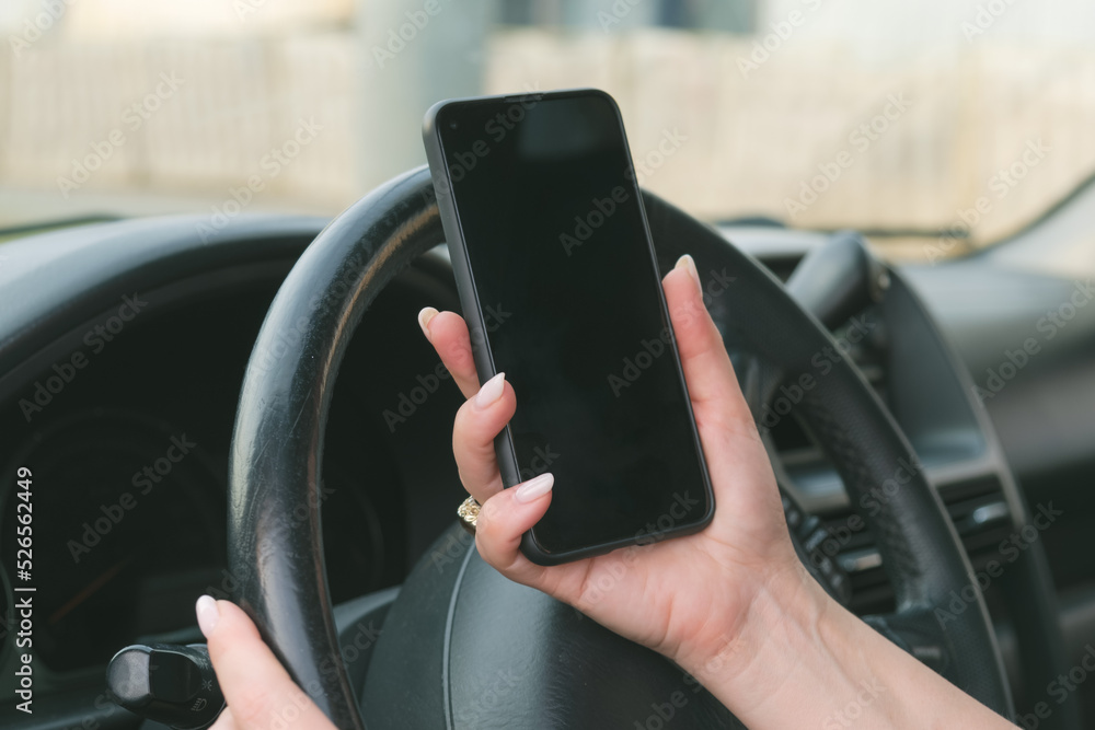 Woman with a manicure holds a smartphone in front of the steering wheel of a car