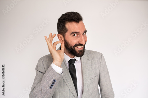Good-looking bearded man making call me gesture. Male model in suit urging to call, touching earlobe. Portrait, studio shot, gesture concept