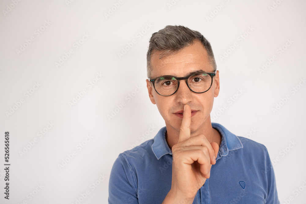 Attractive man in glasses calling be silent. Mid adult male model in T-shirt touching lips with finger, looking at camera. Portrait, studio shot, gesture concept Attractive man in glasses calling be silent. Mid adult male model in T-shirt touching lips with finger, looking at camera. Portrait, studio shot, gesture concept
