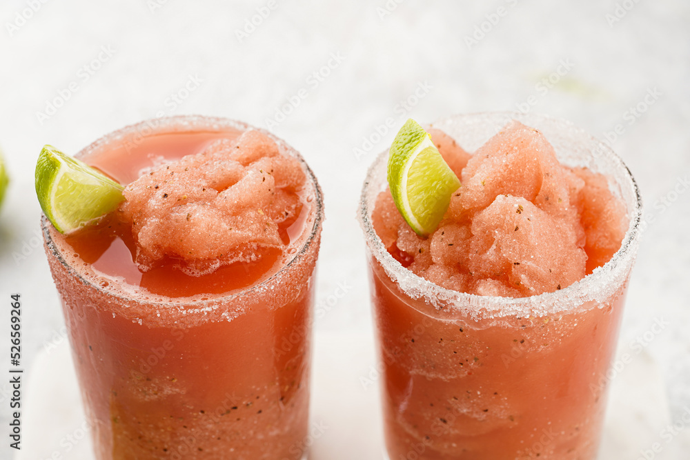 Two glasses with tall long watermelon drink with crushed ice, sugar rims, lime slices on marble board on grey background, close-up Two glasses with tall long watermelon drink with crushed ice, sugar rims, lime slices on marble board on grey background, close-up