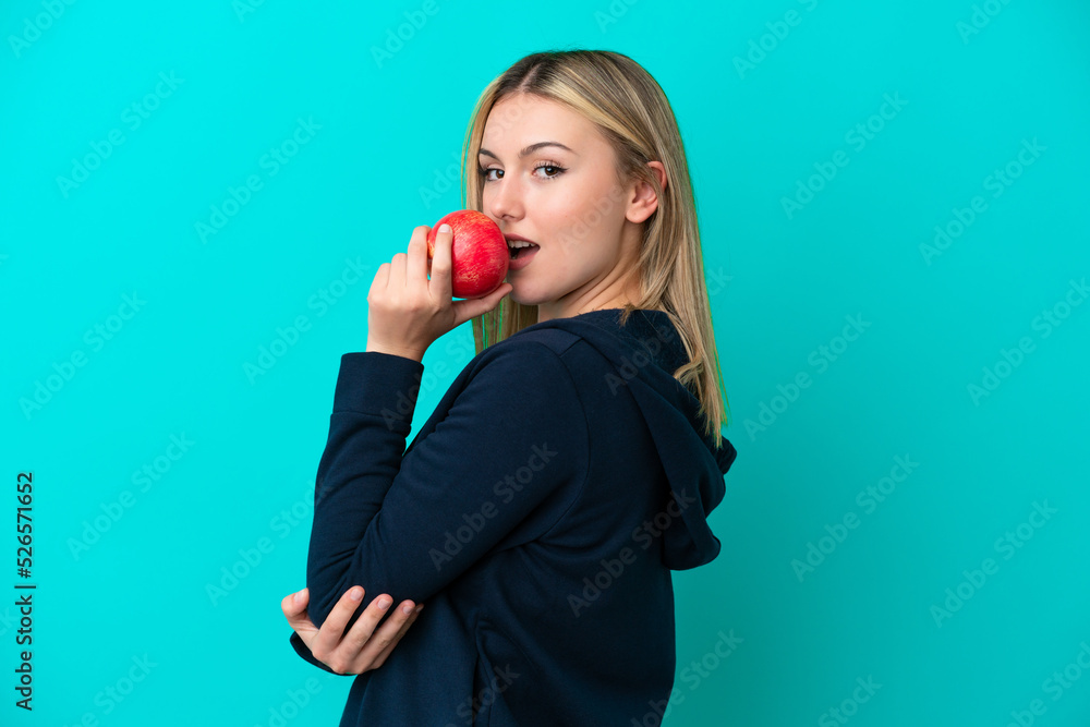 Young caucasian woman isolated on blue background eating an apple