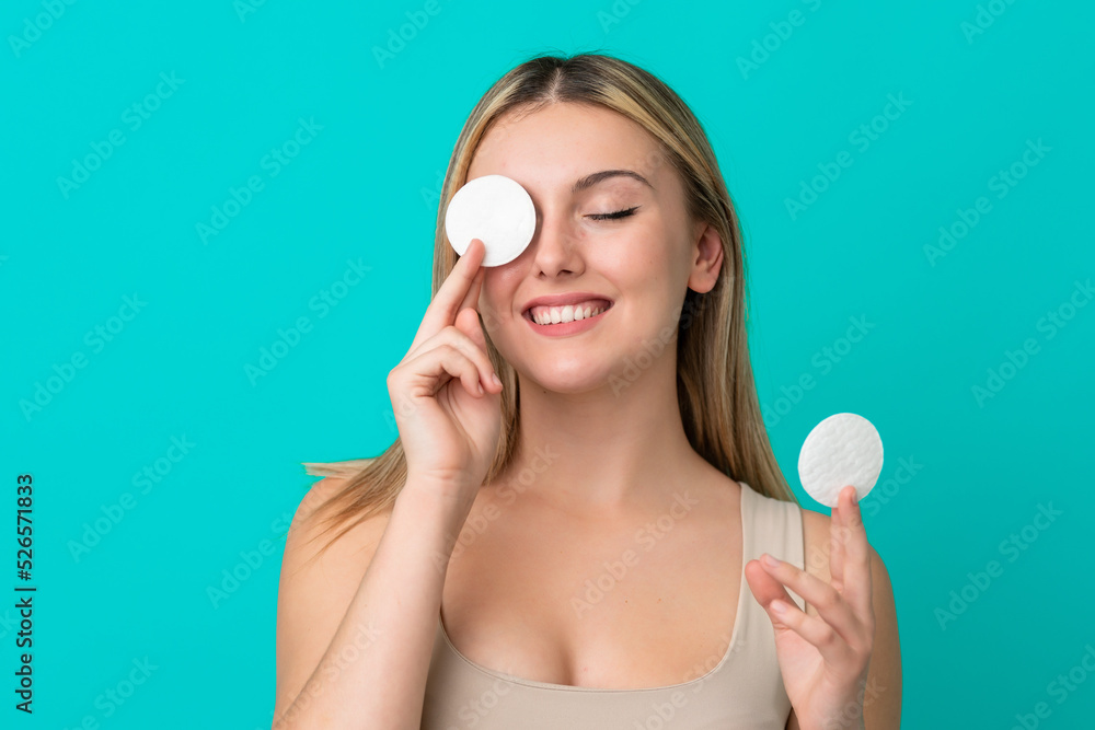 Young caucasian woman isolated on blue background with cotton pad for removing makeup from her face and smiling Young caucasian woman isolated on blue background with cotton pad for removing makeup from her face and smiling