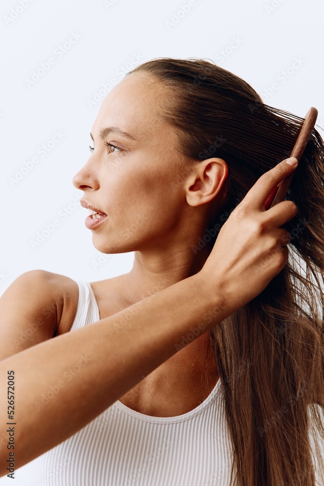 Naklejka premium A woman with long brown hair stands back and takes care of her hair after washing and combing her hair with a wooden comb. Healthy hair without hair loss