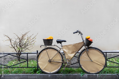 A wet orange pumpkin in a black wicker basket of a ghost bike and a tree in the rain. Side view. Space for text.