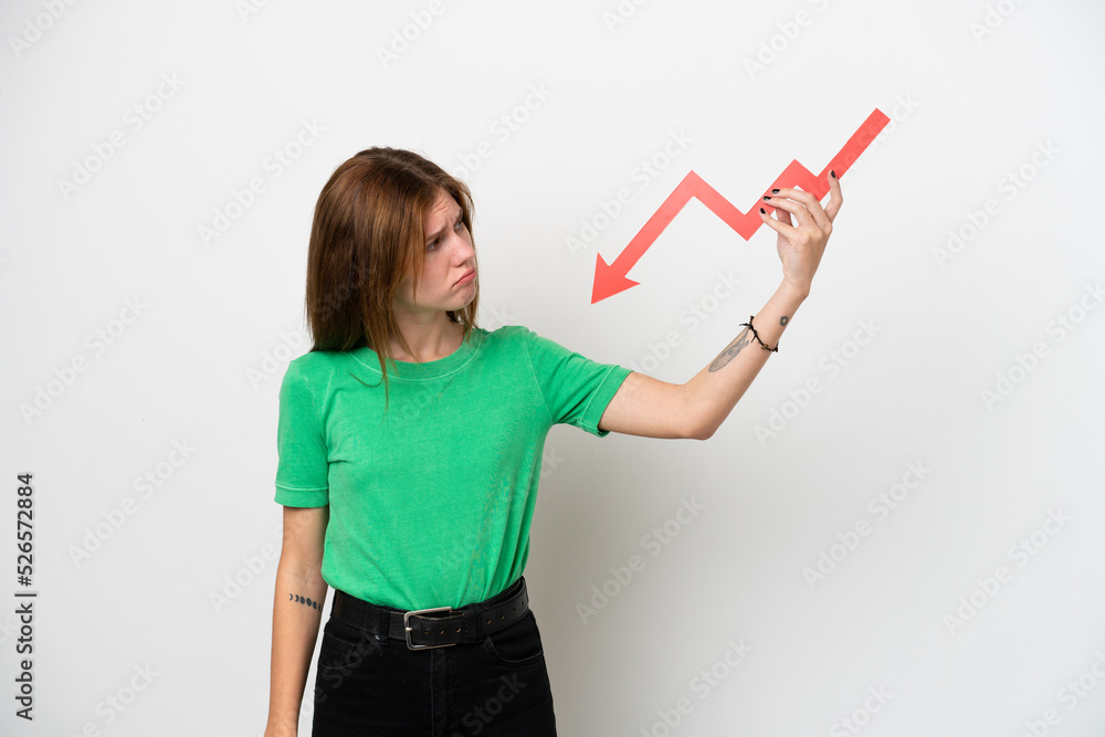 Young English woman isolated on white background holding a downward arrow and with sad expression Young English woman isolated on white background holding a downward arrow and with sad expression