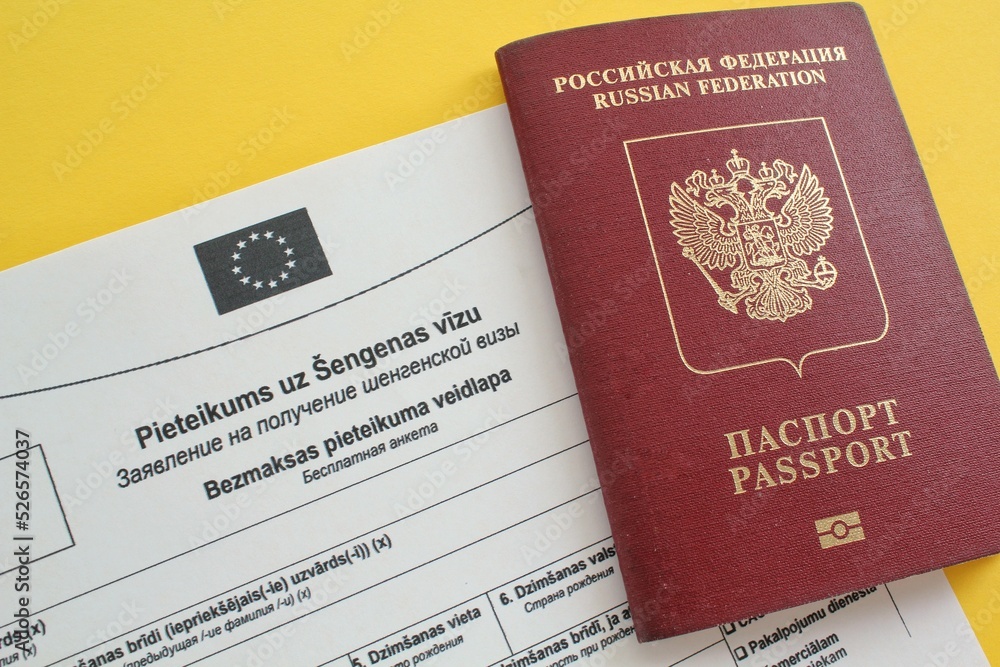 Schengen visa application form in Russian and Latvian language and passport on yellow background. Prohibition and suspension of visas for tourists to travel to European Union and Baltic States concept Schengen visa application form in Russian and Latvian language and passport on yellow background. Prohibition and suspension of visas for tourists to travel to European Union and Baltic States concept