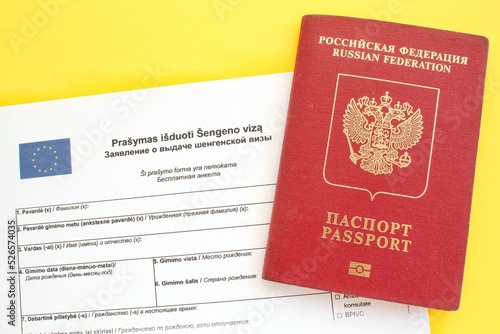 Schengen visa application form in Russian and Lithuanian language and passport on yellow background. Prohibition and suspension of visas for tourists travel to European Union and Baltic States